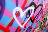 Multiple colorful hearts in white, black, and red are painted on a vibrant background of pink, blue, and purple with graffiti-style designs.