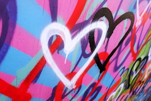 Multiple colorful hearts in white, black, and red are painted on a vibrant background of pink, blue, and purple with graffiti-style designs.