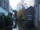 Aerial view of a quiet canal winding through a historic town, framed by autumn trees.