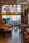 A stylish and modern restaurant interior with wooden accents and ample seating. Large windows provide a view of the cityscape outside, allowing natural light to fill the space. Hanging lights with a unique design add to the contemporary ambiance. Tables are set with dishes and glassware, ready for guests.