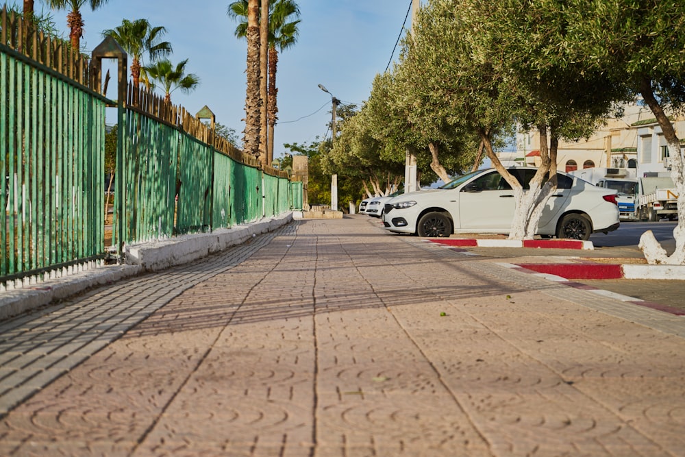 a street lined with parked cars next to a green fence