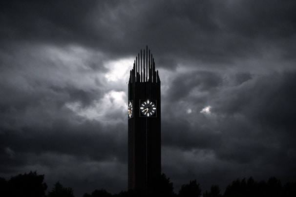 Softly lit image of an old clock tower, its hands frozen at a moment long past, shadowed beneath stormy skies.