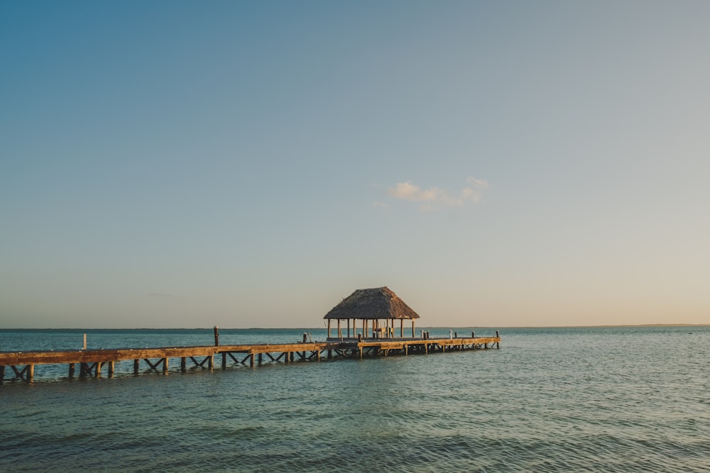 a pier with a hut on top of it in the middle of the ocean