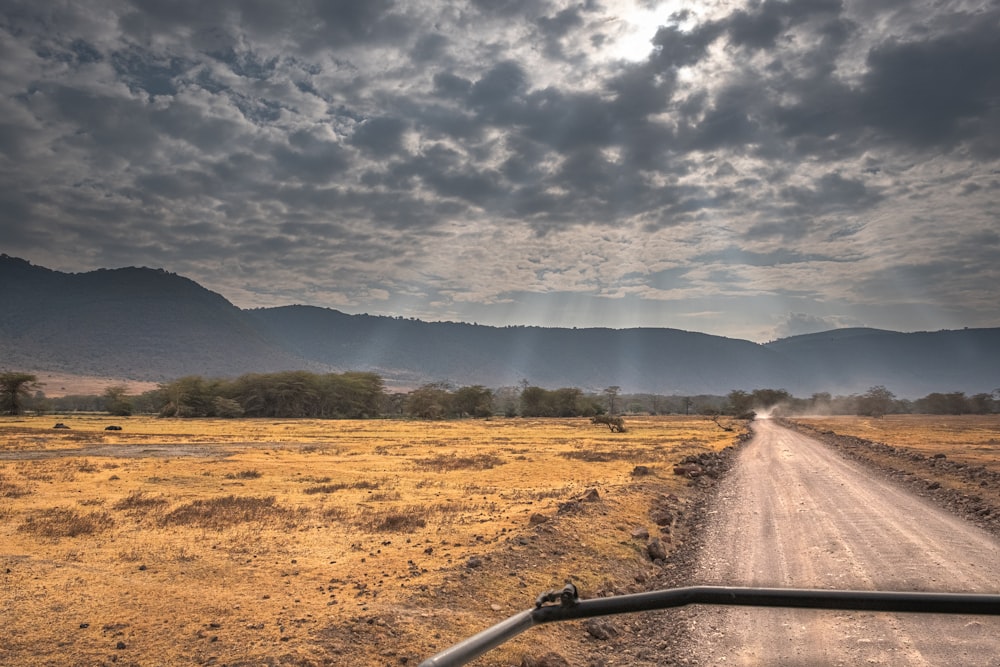 a truck driving down a dirt road under a cloudy sky