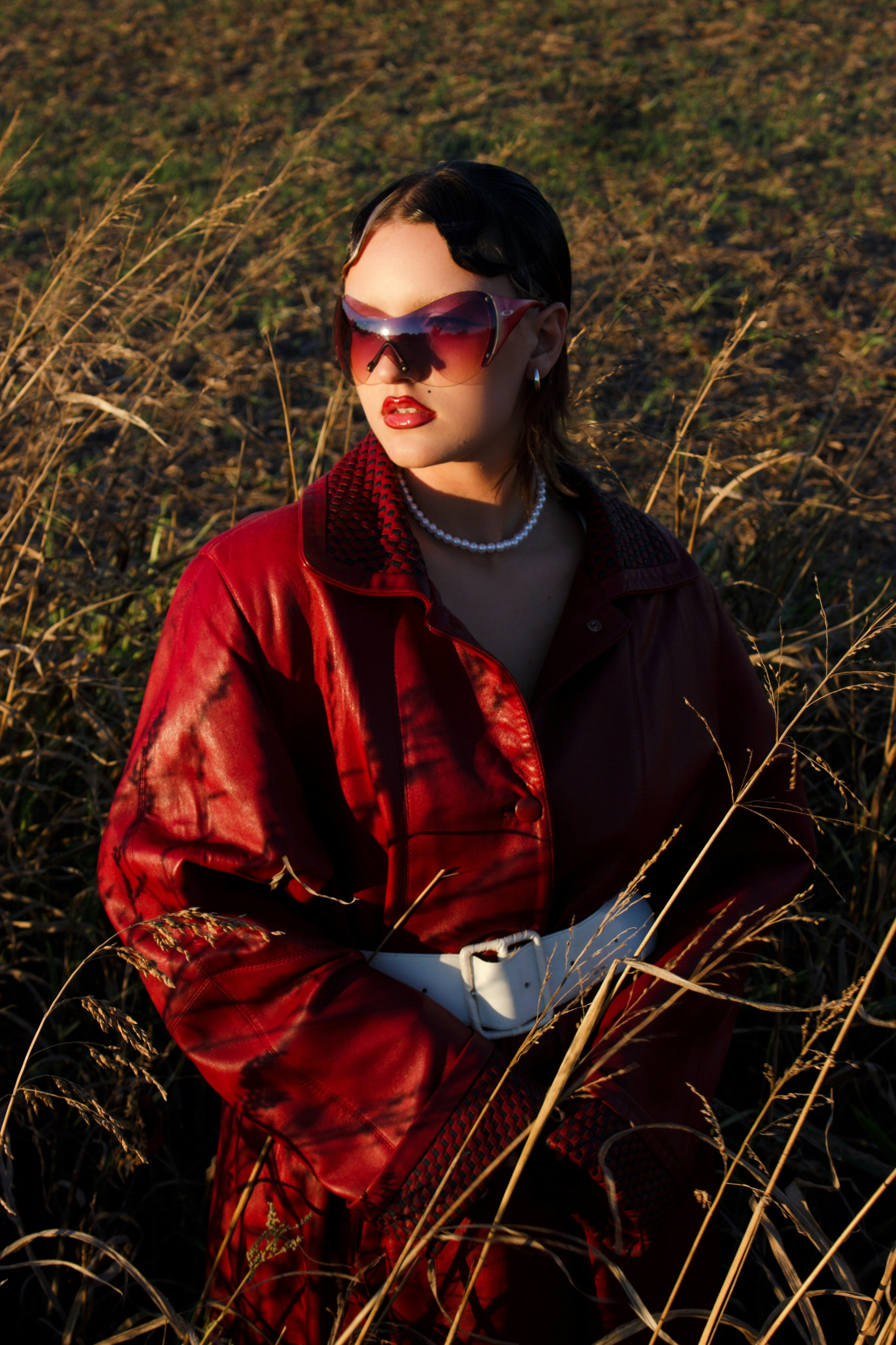 a woman in a red coat and sunglasses standing in a field
