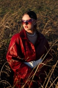 a woman in a red coat and sunglasses standing in a field