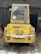 A yellow industrial vehicle is parked in a barn-like structure with its rear facing the viewer. The vehicle is labeled 'Kramer Allrad 312 SL' and has a number '20' sticker in the window. The vehicle is surrounded by some snow and hay on the ground, and there are wooden beams and a dark interior visible in the background.