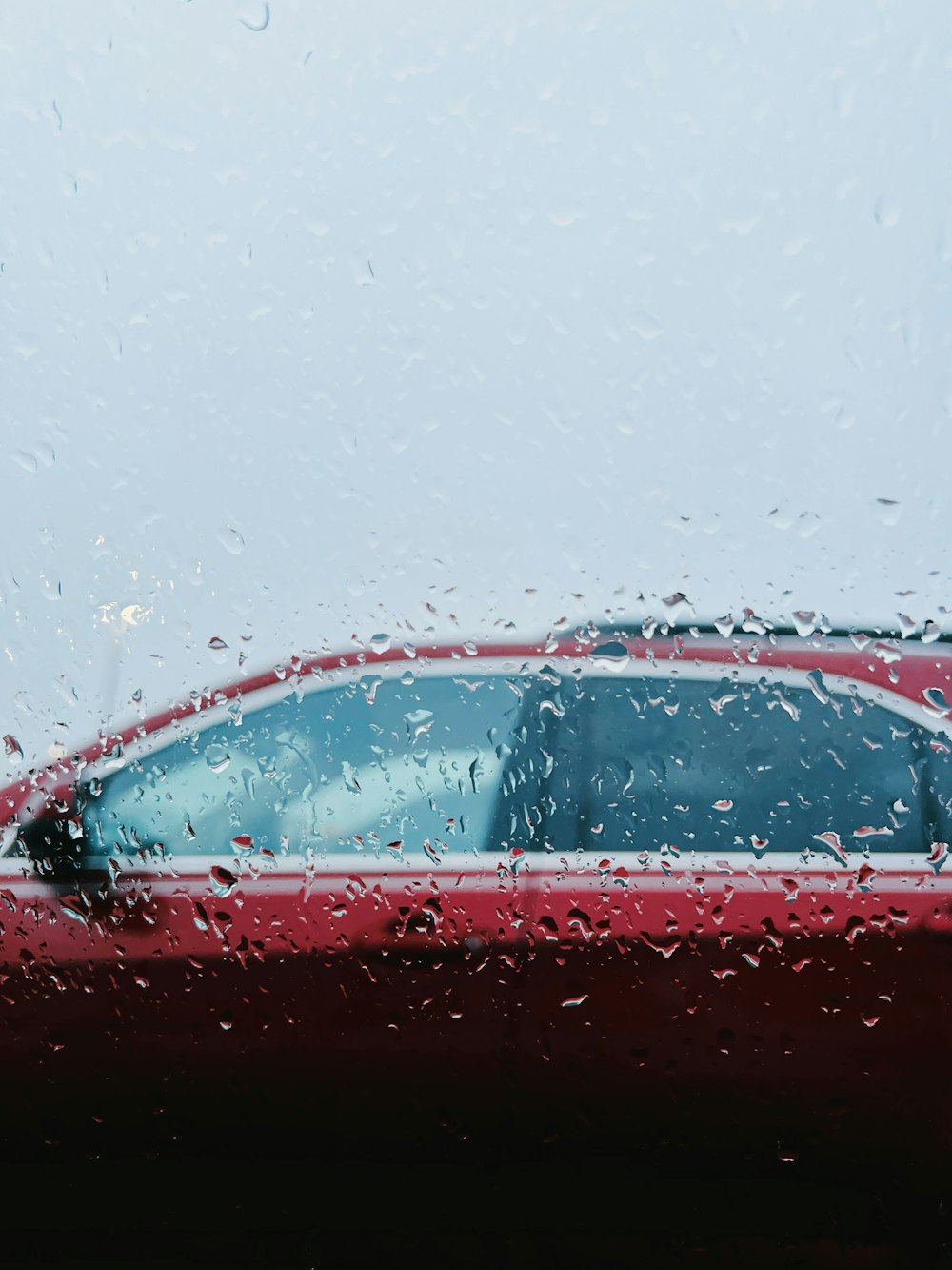 a red car is seen through a rain soaked window