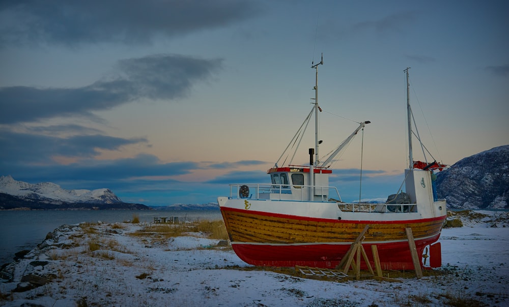 a red and white boat sitting on top of snow covered ground