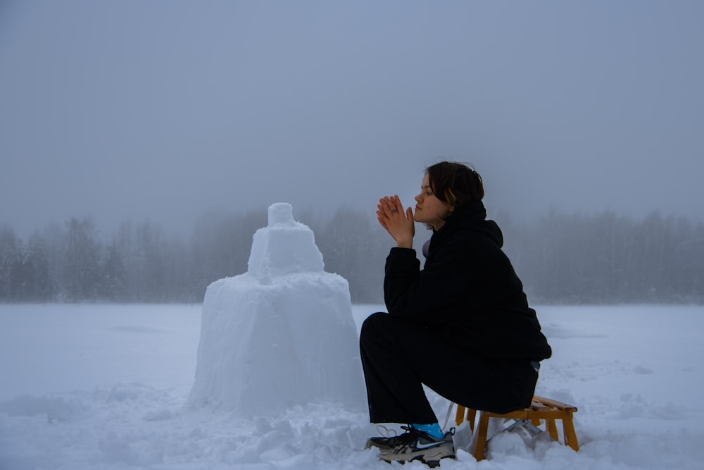 a person sitting on a bench next to a snow man