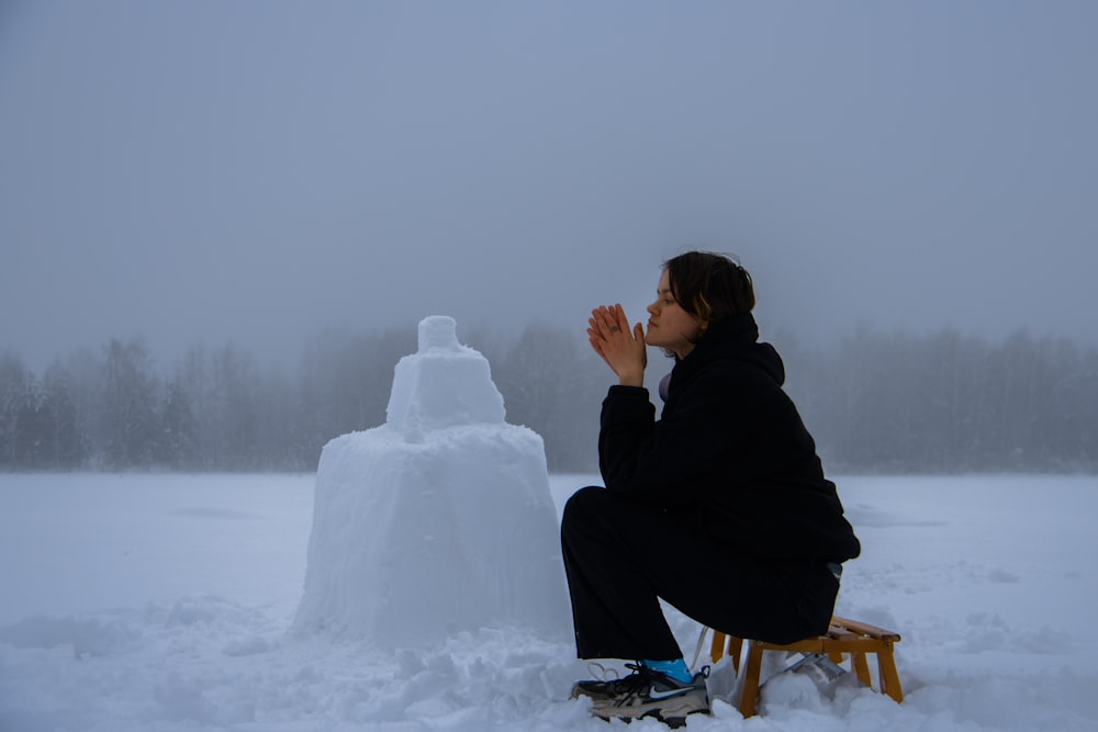 una persona seduta su una panchina accanto a un pupazzo di neve