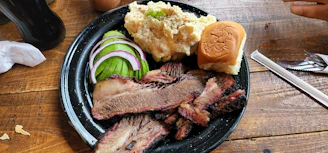 A neatly packed takeout box filled with smoked meats and classic Texas sides, set against a green and black background.
