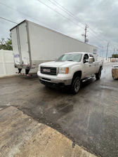 Red pickup truck hitched to a silver trailer parked by a warehouse, ready for a hotshot delivery.
