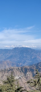 A breathtaking view of a mountain landscape with a clear blue sky and rolling hills in the foreground.