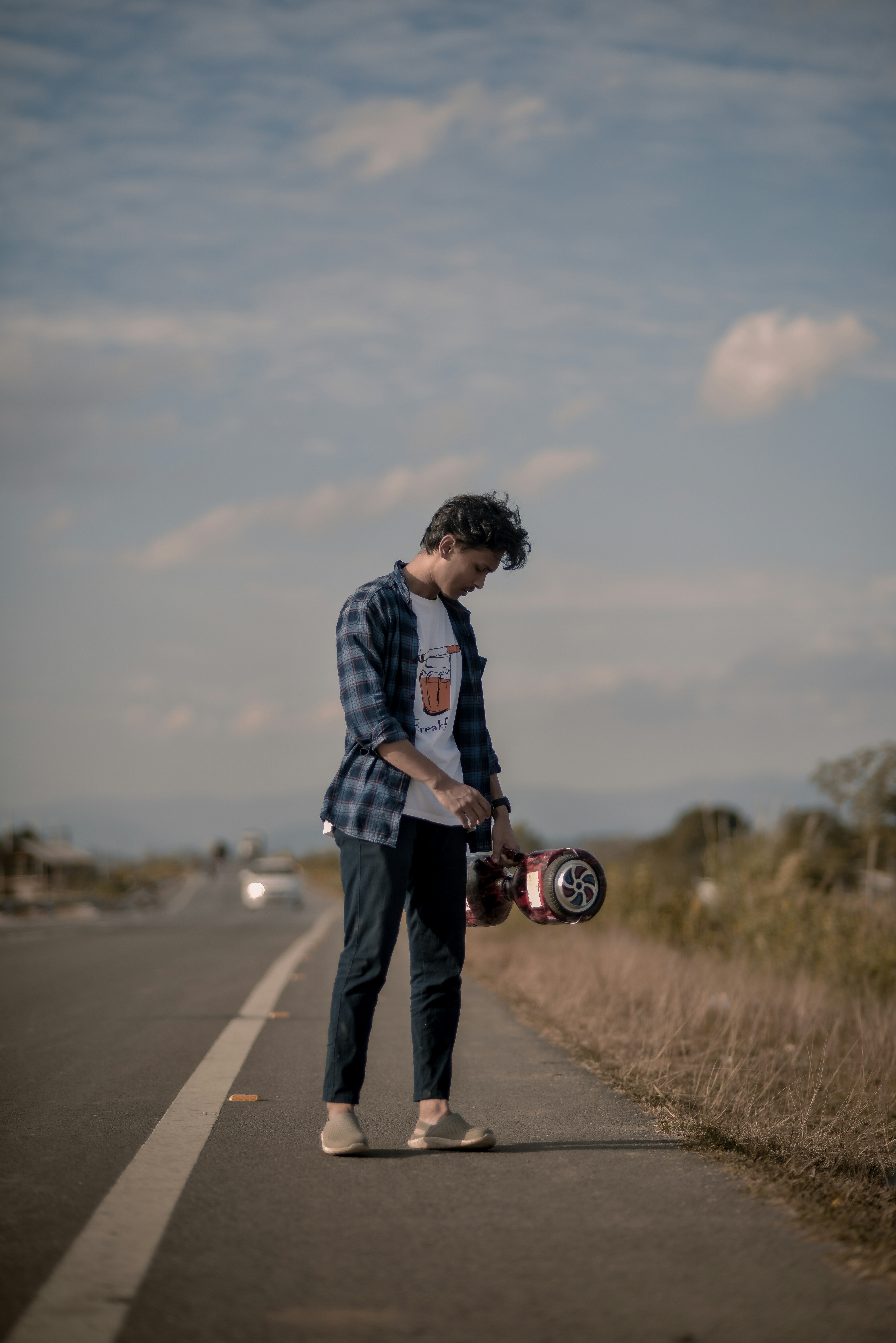 a man standing on the side of a road holding a skateboard