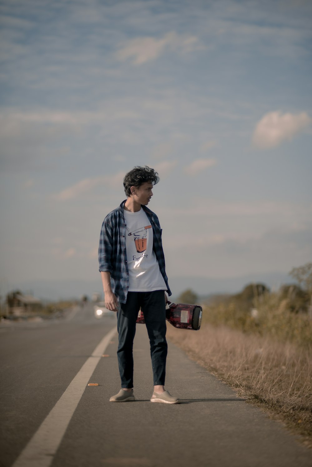 a man standing on the side of a road holding a skateboard