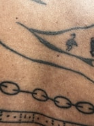 A close-up view of a section of human skin with black ink tattoo designs, including lines, dots, and abstract geometric patterns.