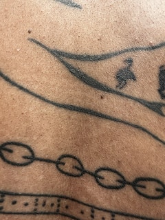 A close-up view of a section of human skin with black ink tattoo designs, including lines, dots, and abstract geometric patterns.