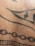 A close-up view of a section of human skin with black ink tattoo designs, including lines, dots, and abstract geometric patterns.