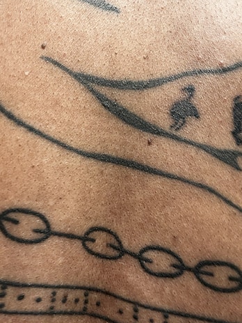 A close-up view of a section of human skin with black ink tattoo designs, including lines, dots, and abstract geometric patterns.