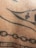 A close-up view of a section of human skin with black ink tattoo designs, including lines, dots, and abstract geometric patterns.