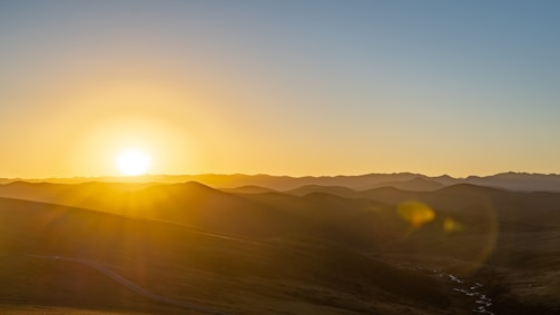 A serene landscape photo capturing golden hour light over rolling hills.