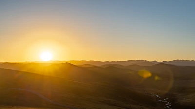 A serene landscape at sunset with warm golden light casting long shadows over rolling hills.
