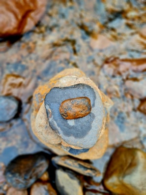 Smooth stones with earthy tones are stacked on top of each other, surrounded by water. The stones vary in size and color, with a prominent dark stone on top.