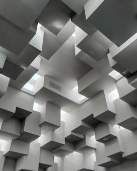 An abstract architectural design featuring numerous geometric, three-dimensional cubes protruding from a ceiling. The cubes are arranged in a seemingly random but artistic pattern, creating a complex visual effect. The lighting emphasizes the depth and structure, casting shadows that enhance the overall architectural aesthetic.