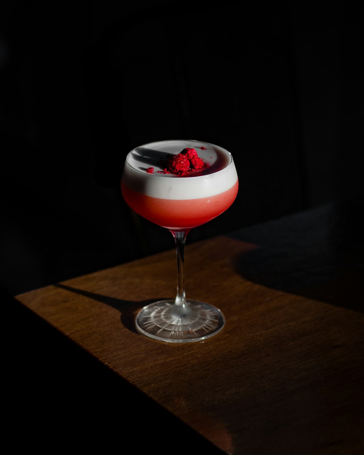 A clover club cocktail with raspberries in a coupe glass