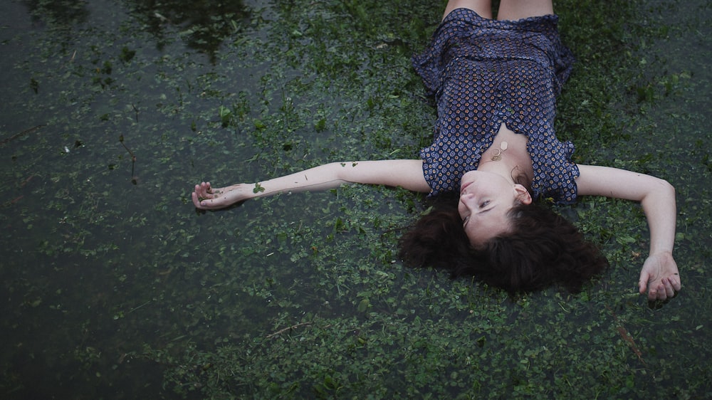 uma mulher deitada no chão ao lado de um corpo de água