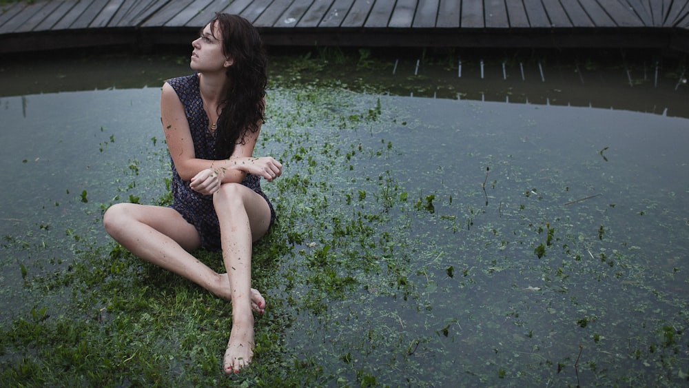 a woman sitting on the ground next to a body of water