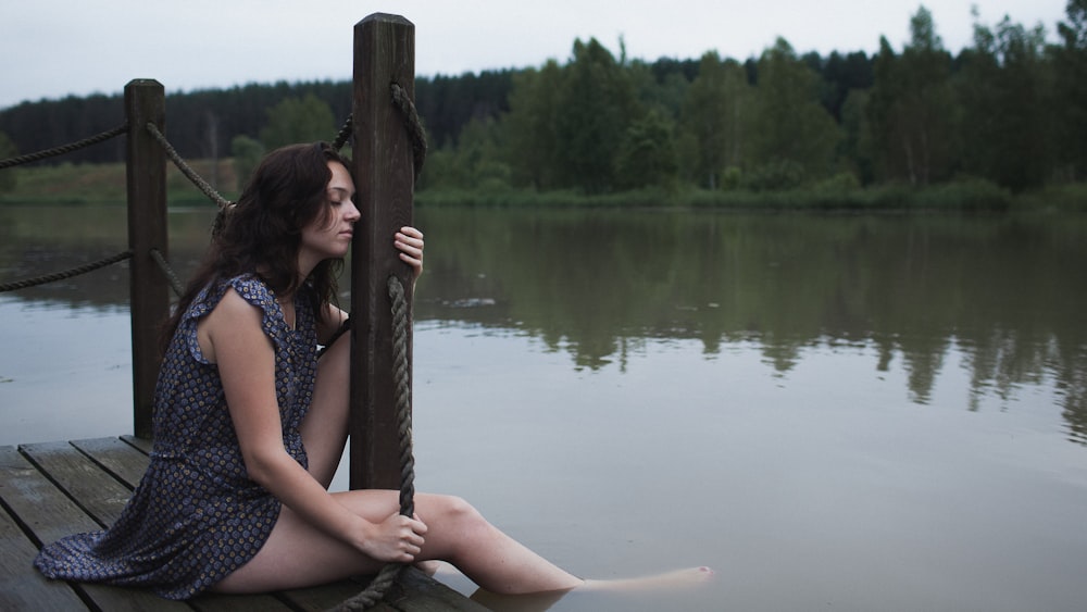 a woman sitting on a dock next to a body of water