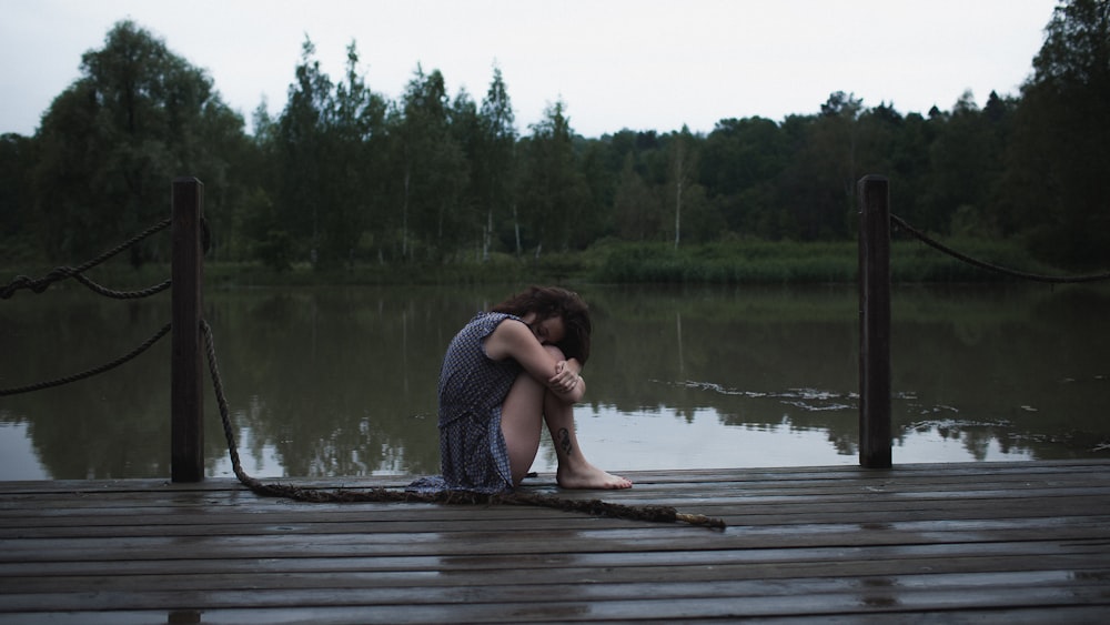 a woman sitting on a dock with her head in her hands