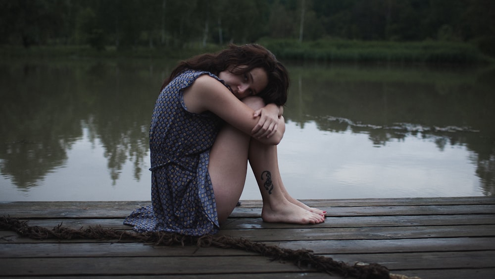 a woman sitting on a dock next to a body of water