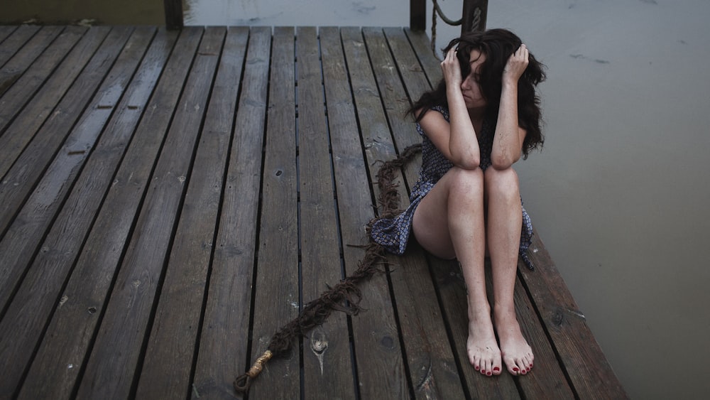 a woman sitting on a dock with her head in her hands