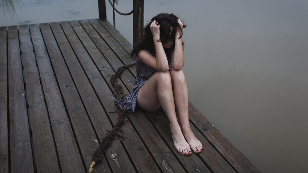 a woman sitting on a dock with her head in her hands