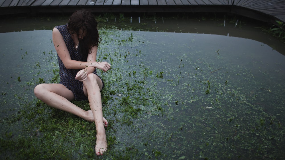 a woman sitting on the ground next to a body of water