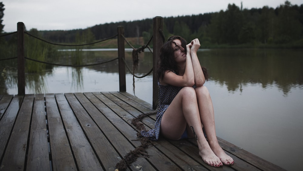 a woman sitting on a dock in front of a body of water