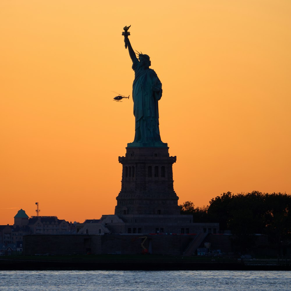 the statue of liberty is silhouetted against an orange sky