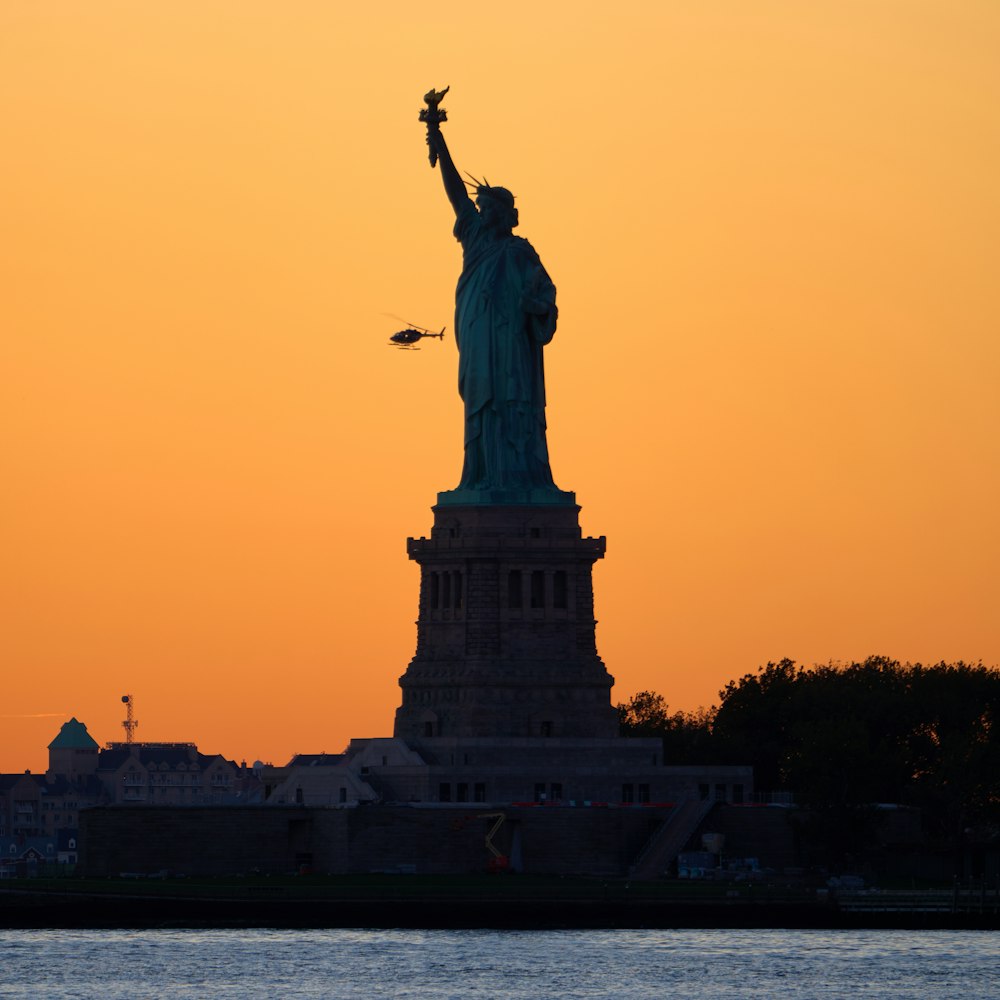 Die Freiheitsstatue ist eine Silhouette vor einem orangefarbenen Himmel