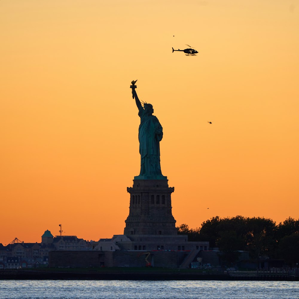 a helicopter flying over the statue of liberty at sunset