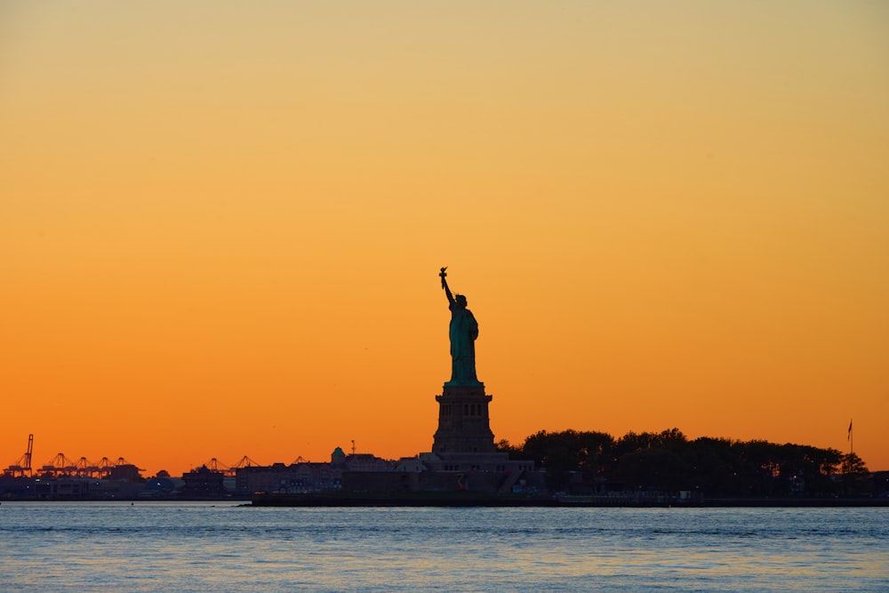 Die Freiheitsstatue ist eine Silhouette vor einem orangefarbenen Himmel