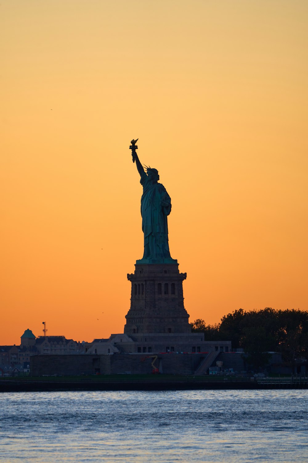 the statue of liberty is silhouetted against an orange sky
