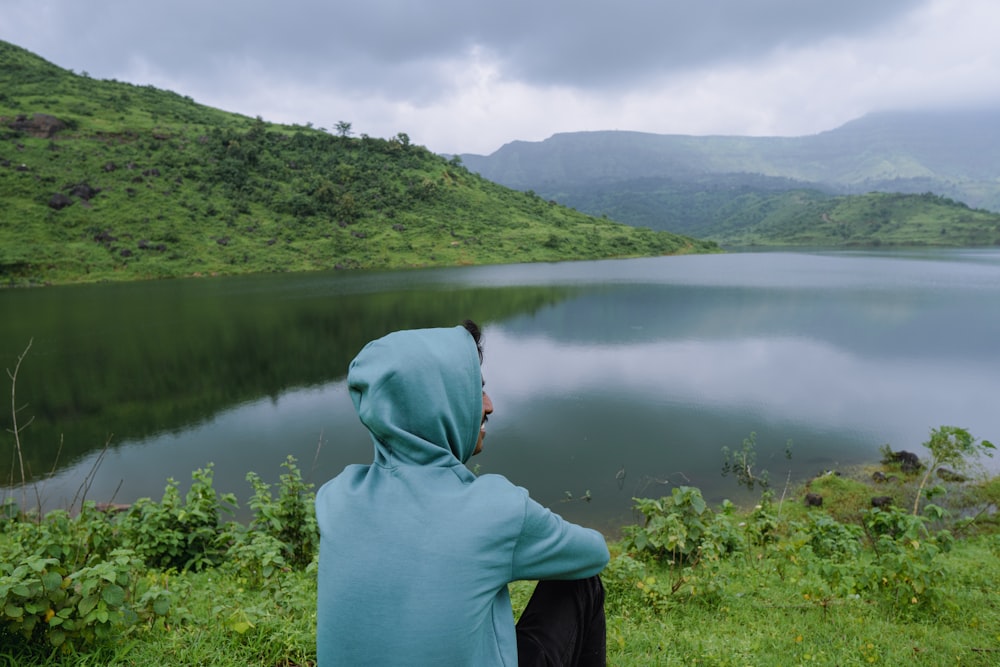 a person in a blue hoodie looking at a lake