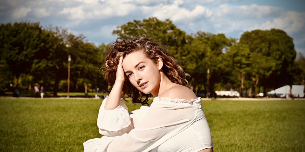 a woman sitting in the grass with her hand on her head