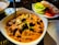 A dish of rich, creamy curry with chunks of meat, garnished with herbs and spices. Accompanying the curry is a side plate of sliced cucumbers, tomatoes, and onions, adding a fresh contrast. The setting suggests an appetizing dining experience.