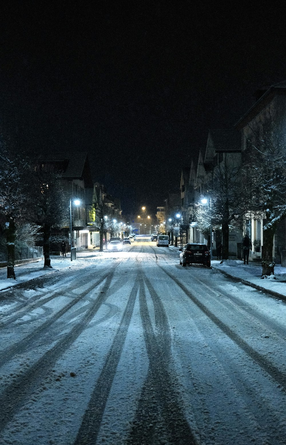 a snow covered street at night with cars parked on the side of the road
