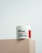 A jar of Naite Thread Neck Cream by MEDI-PEEL rests on a beige platform. The label displays information about the product, which includes enhancing skin elasticity with collagen and peptides. The background is a light, neutral shade which gives a minimalist and clean appearance.