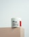 A jar of Naite Thread Neck Cream by MEDI-PEEL rests on a beige platform. The label displays information about the product, which includes enhancing skin elasticity with collagen and peptides. The background is a light, neutral shade which gives a minimalist and clean appearance.